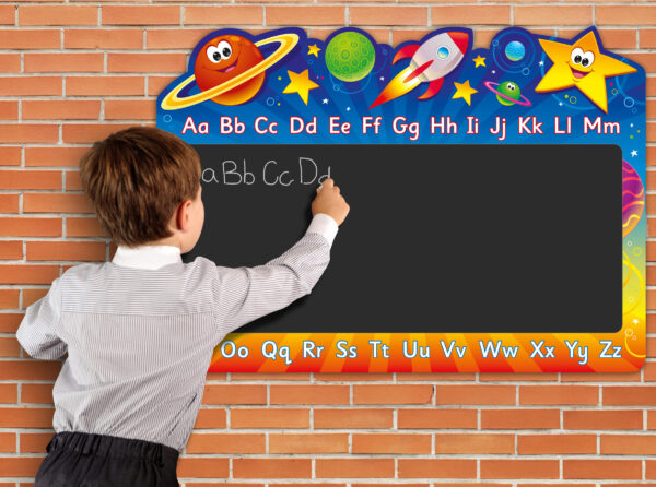 Male child to left of image, writing onto sign. The sign is colourful space themed illustrations. Including planets with friendly faces. English alphabet A to Z, top and bottom of black chalkboard that is within the central area of the sign.